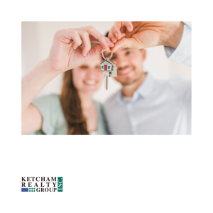 A smiling couple holding a key with a house-shaped keychain, celebrating the final step of their home-buying journey. The Ketcham Realty Group logo is in the lower-left corner.